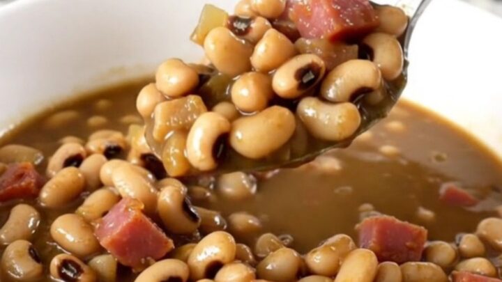 A white bowl filled with black-eyed peas, diced ham, and onion in a savory, thick broth.