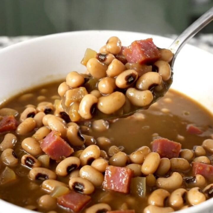 A white bowl filled with black-eyed peas, diced ham, and onion in a savory, thick broth.