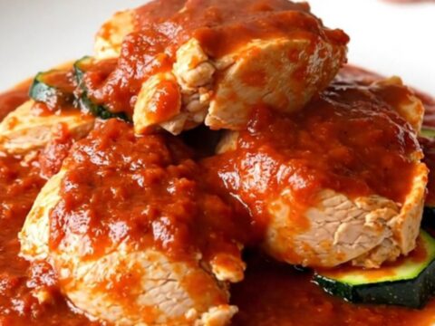 A top-down view of a slow cooker filled with tender chicken thighs, zucchini coins, and rich red marinara sauce.