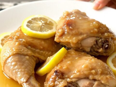 A top-down view of tender honey lemon chicken thighs in a slow cooker with thin lemon slices.
