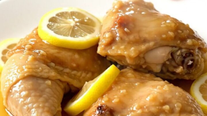 A top-down view of tender honey lemon chicken thighs in a slow cooker with thin lemon slices.