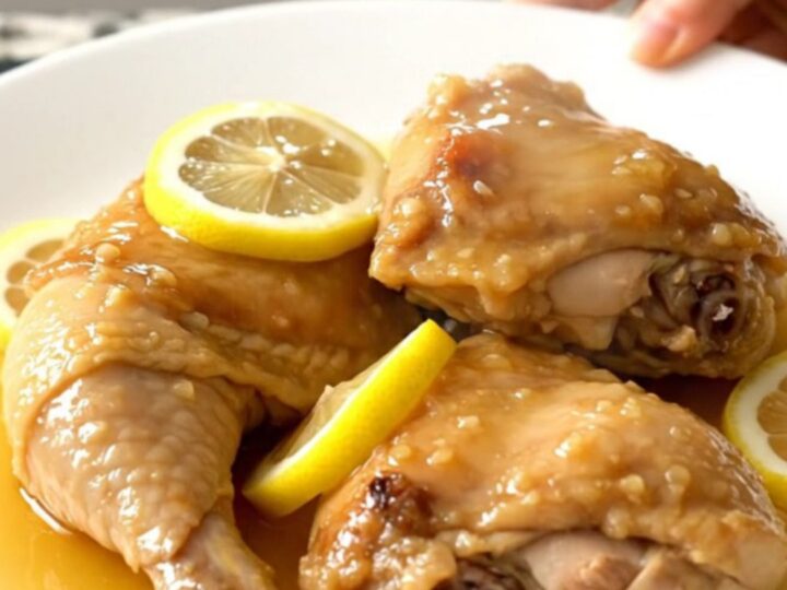 A top-down view of tender honey lemon chicken thighs in a slow cooker with thin lemon slices.