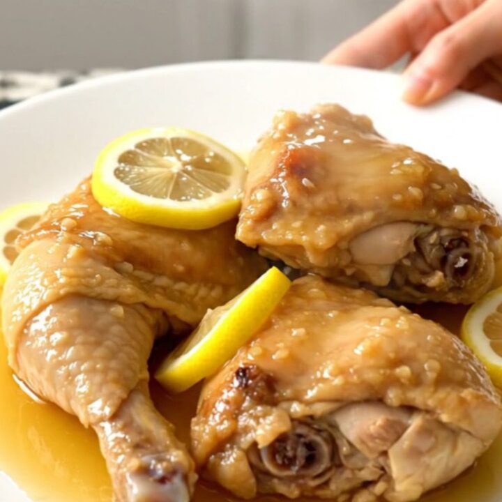 A top-down view of tender honey lemon chicken thighs in a slow cooker with thin lemon slices.