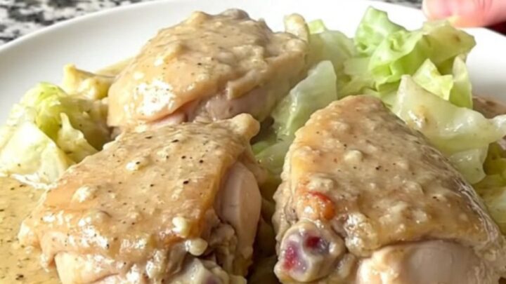 A top-down view of chicken thighs and cabbage wedges in a creamy sauce inside a black slow cooker.