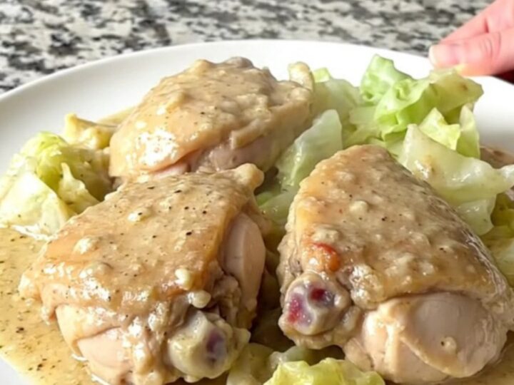 A top-down view of chicken thighs and cabbage wedges in a creamy sauce inside a black slow cooker.