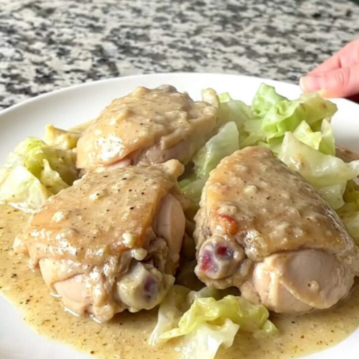 A top-down view of chicken thighs and cabbage wedges in a creamy sauce inside a black slow cooker.