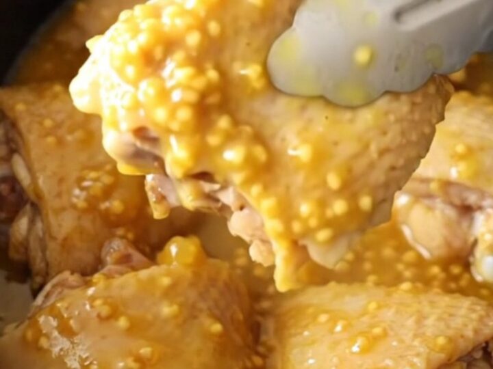 A close-up of tender, glazed chicken thighs in a slow cooker with a thick pineapple and mustard sauce.