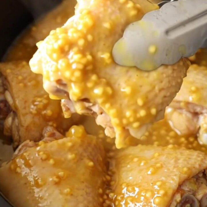 A close-up of tender, glazed chicken thighs in a slow cooker with a thick pineapple and mustard sauce.