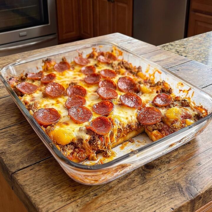 A thick, steaming slice of meat lovers pizza casserole being lifted from a glass dish with a spatula.