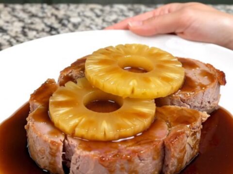 A close-up of thick, glazed ham steaks topped with pineapple rings, served on a white plate.