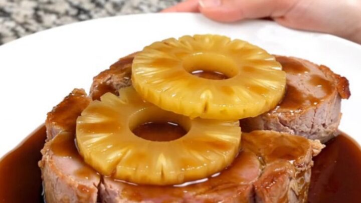 A close-up of thick, glazed ham steaks topped with pineapple rings, served on a white plate.