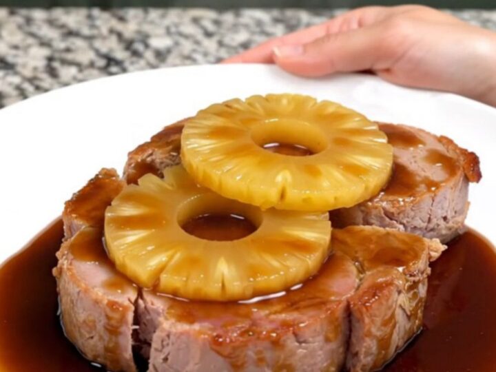 A close-up of thick, glazed ham steaks topped with pineapple rings, served on a white plate.