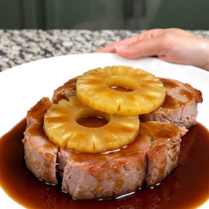 A close-up of thick, glazed ham steaks topped with pineapple rings, served on a white plate.