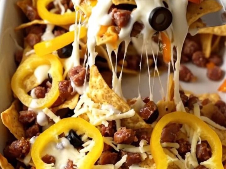 A top-down view of a rectangular baking dish filled with tortilla chips, sausage, Alfredo sauce, and melted cheese.