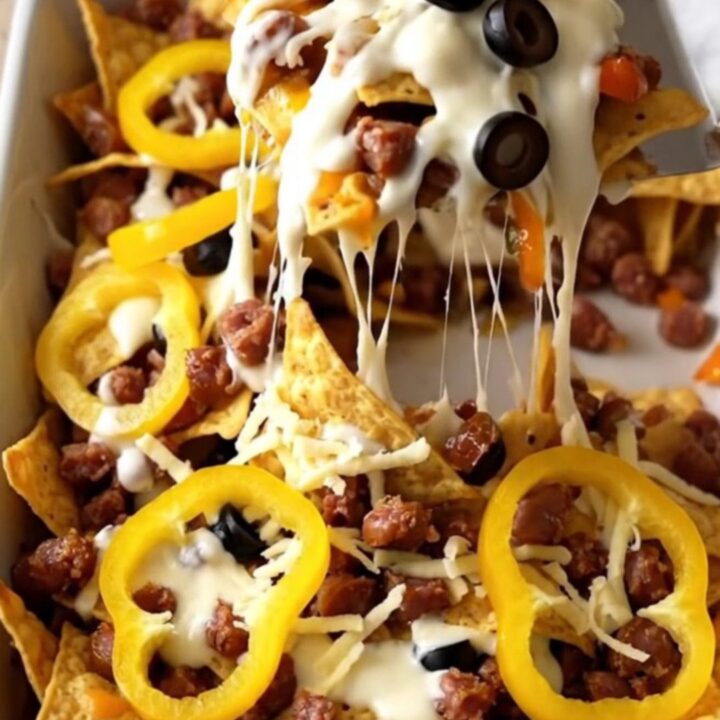 A top-down view of a rectangular baking dish filled with tortilla chips, sausage, Alfredo sauce, and melted cheese.