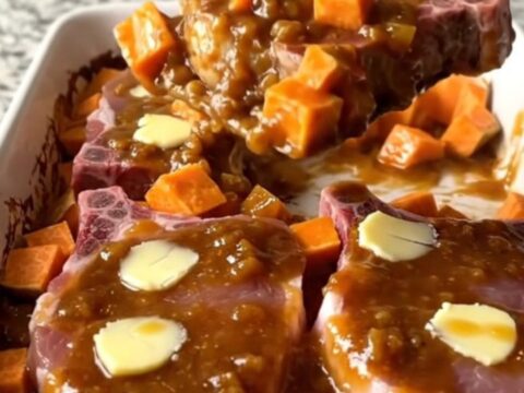A large ceramic dish filled with roasted pork chops and sweet potatoes coated in a thick, glossy apple butter glaze.