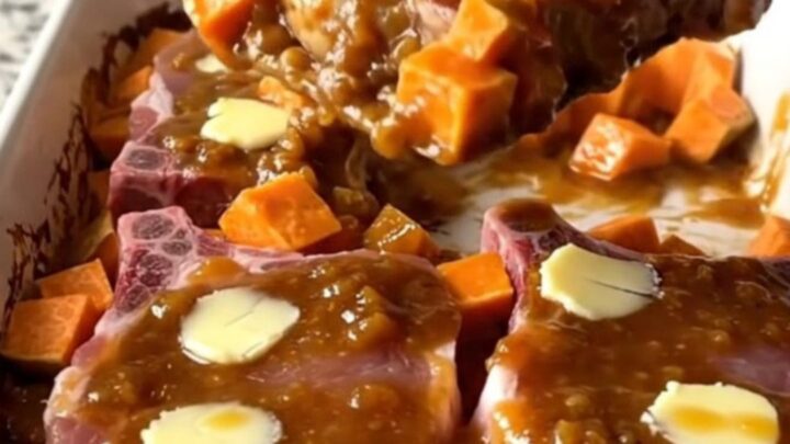 A large ceramic dish filled with roasted pork chops and sweet potatoes coated in a thick, glossy apple butter glaze.