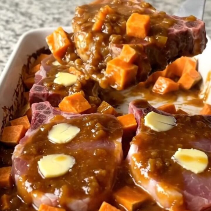 A large ceramic dish filled with roasted pork chops and sweet potatoes coated in a thick, glossy apple butter glaze.