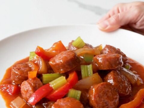 A close-up of a bowl filled with sliced andouille sausage, colorful bell peppers, and onions in a rich tomato sauce.