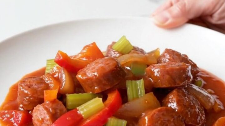 A close-up of a bowl filled with sliced andouille sausage, colorful bell peppers, and onions in a rich tomato sauce.