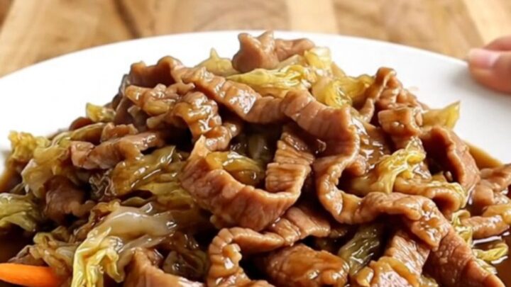 A slow cooker filled with tender strips of pork, shredded cabbage, and carrots in a rich, dark hoisin sauce.