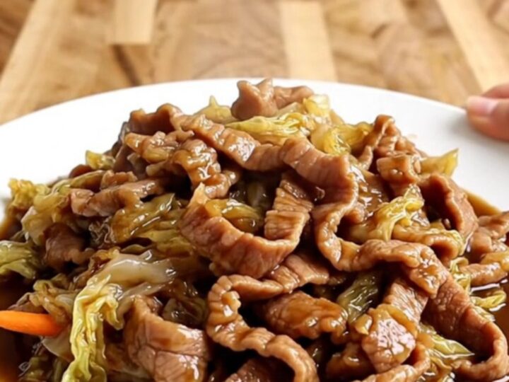 A slow cooker filled with tender strips of pork, shredded cabbage, and carrots in a rich, dark hoisin sauce.