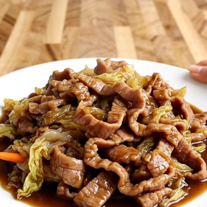 A slow cooker filled with tender strips of pork, shredded cabbage, and carrots in a rich, dark hoisin sauce.