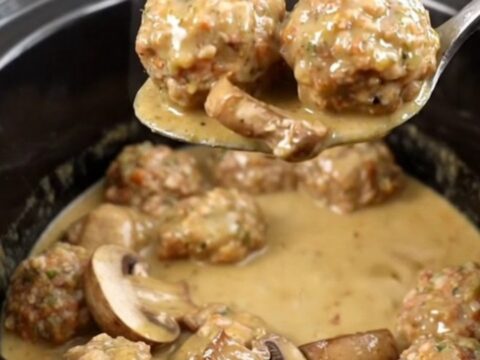 A slow cooker filled with chicken meatballs and mushrooms in a creamy tan Marsala sauce.