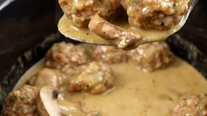A slow cooker filled with chicken meatballs and mushrooms in a creamy tan Marsala sauce.