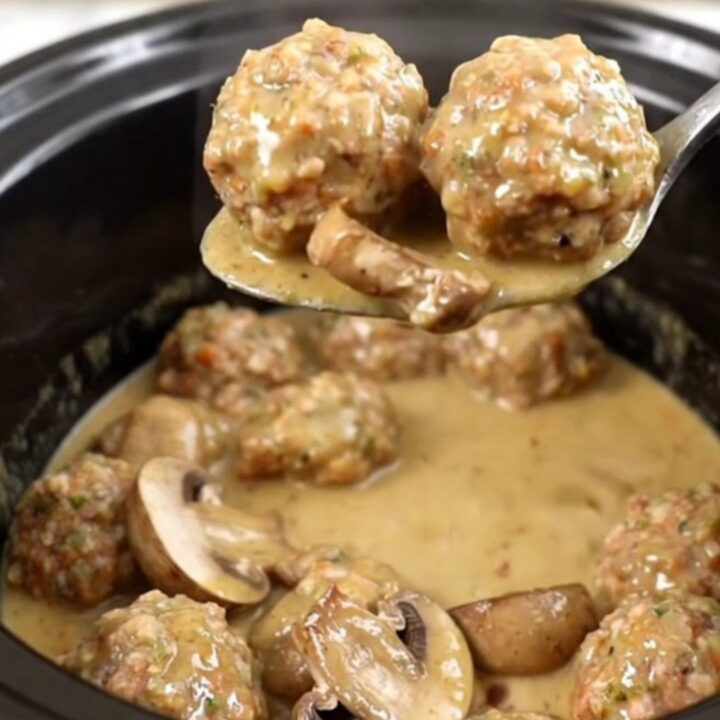 A slow cooker filled with chicken meatballs and mushrooms in a creamy tan Marsala sauce.