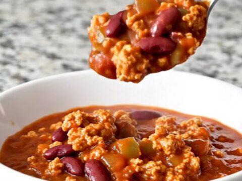 A rustic bowl of hearty red turkey chili with visible beans and peppers, garnished with fresh herbs.