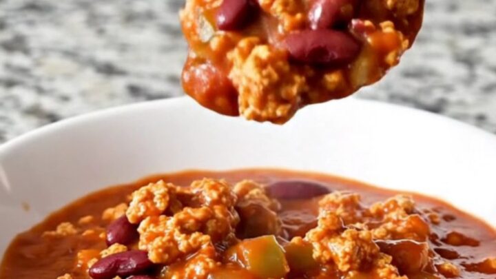 A rustic bowl of hearty red turkey chili with visible beans and peppers, garnished with fresh herbs.
