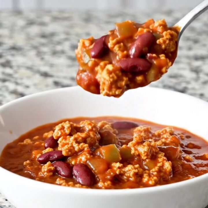 A rustic bowl of hearty red turkey chili with visible beans and peppers, garnished with fresh herbs.