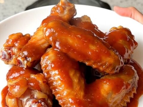 Slow cooker mumbo sauce chicken wings served on a white plate with a glossy red sauce.