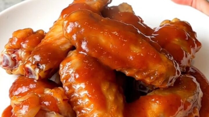 Slow cooker mumbo sauce chicken wings served on a white plate with a glossy red sauce.