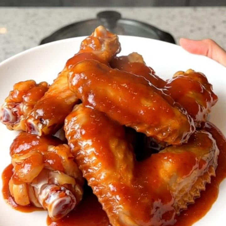 Slow cooker mumbo sauce chicken wings served on a white plate with a glossy red sauce.