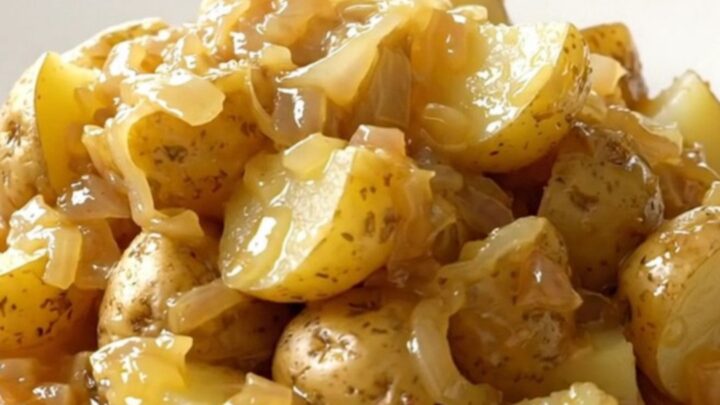 A white plate filled with tender, buttery quartered gold potatoes with onion flecks.