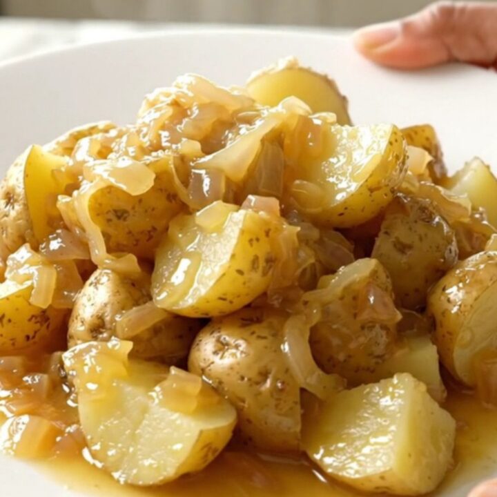 A white plate filled with tender, buttery quartered gold potatoes with onion flecks.