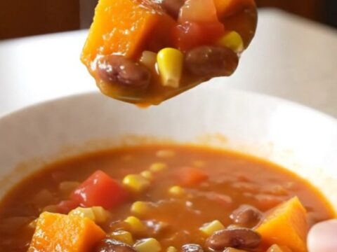 A close-up of a white bowl filled with a vibrant harvest stew featuring cubes of squash, beans