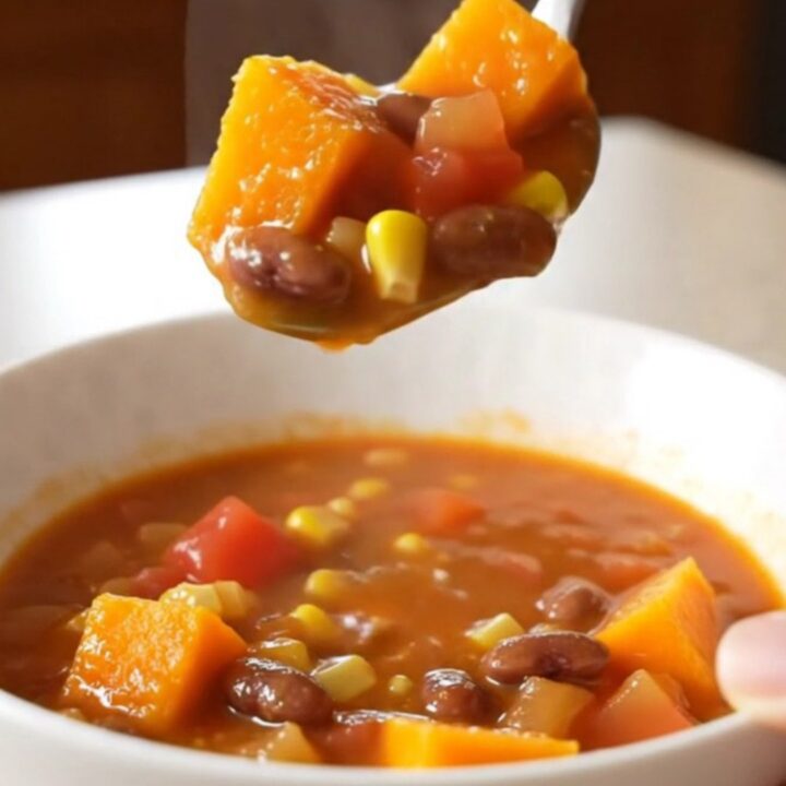 A close-up of a white bowl filled with a vibrant harvest stew featuring cubes of squash, beans