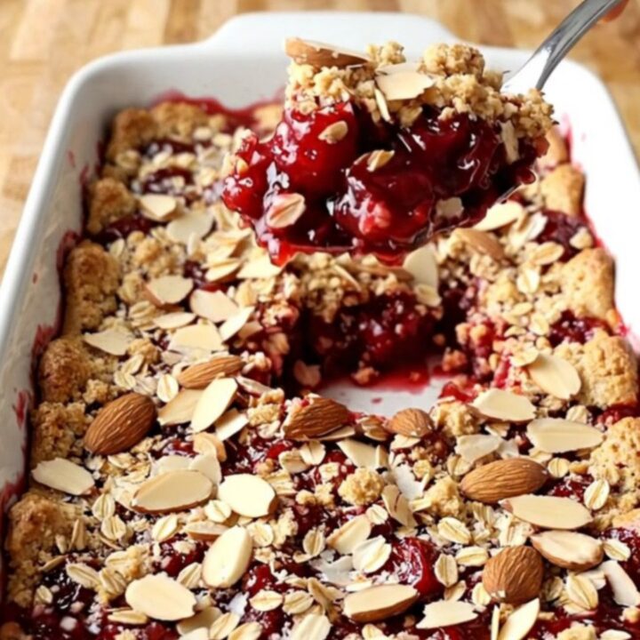 A warm, golden-brown cherry almond crisp in a rectangular white ceramic dish.