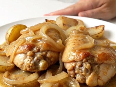 Slow cooker French onion chicken thighs with halved potatoes and a creamy onion sauce served in a white bowl.