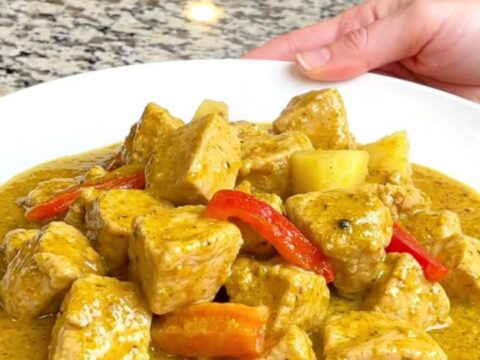 A close-up of tender chicken breast, pineapple chunks, and red bell peppers in a creamy yellow curry sauce.