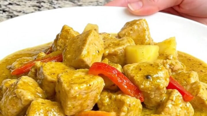 A close-up of tender chicken breast, pineapple chunks, and red bell peppers in a creamy yellow curry sauce.