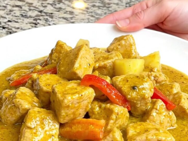 A close-up of tender chicken breast, pineapple chunks, and red bell peppers in a creamy yellow curry sauce.