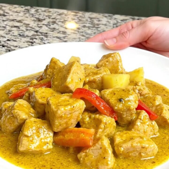 A close-up of tender chicken breast, pineapple chunks, and red bell peppers in a creamy yellow curry sauce.
