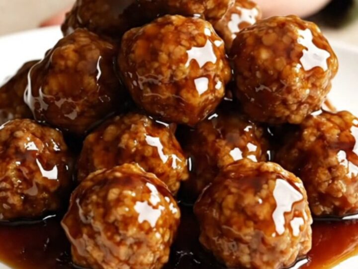 A close-up of honey balsamic meatballs on a white plate, coated in a glossy dark sauce with light steam rising.