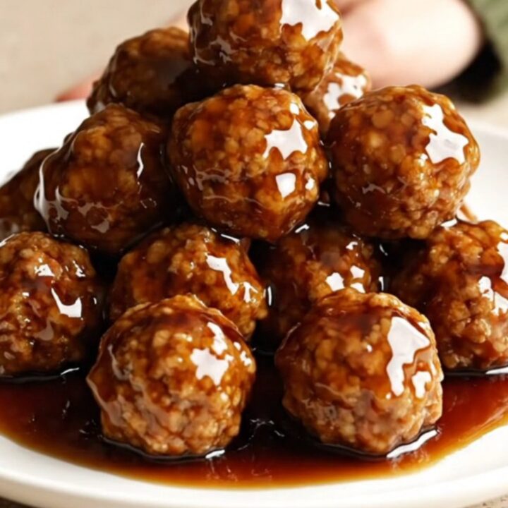 A close-up of honey balsamic meatballs on a white plate, coated in a glossy dark sauce with light steam rising.