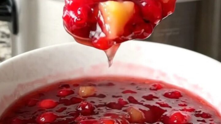 A white bowl filled with vibrant, jammy cranberry pineapple sauce made in a slow cooker.