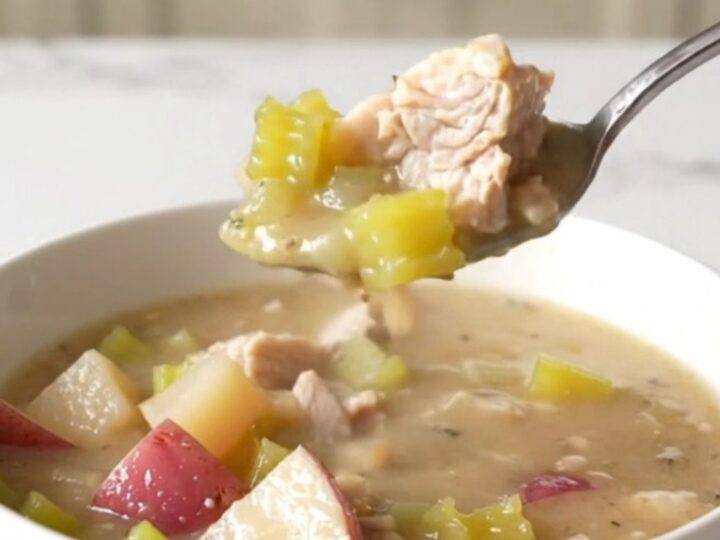 A bowl of creamy chicken and potato chowder with visible chunks of chicken, red potatoes, and celery.